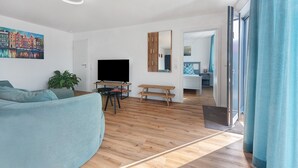 Una sala de estar moderna con sofá, televisor, piso de madera y un cuadro de casas.