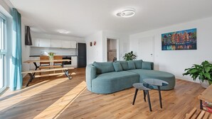 Una sala moderna con un sofá modular, una mesa de comedor y una cocina al fondo.