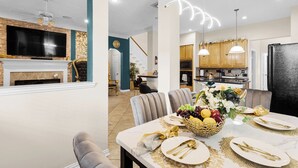 Een eetruimte met een tafel voor vier personen, een open haard en een keuken op de achtergrond.
