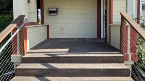 Un espace extérieur abrité, doté d’un escalier en bois menant à une porte.