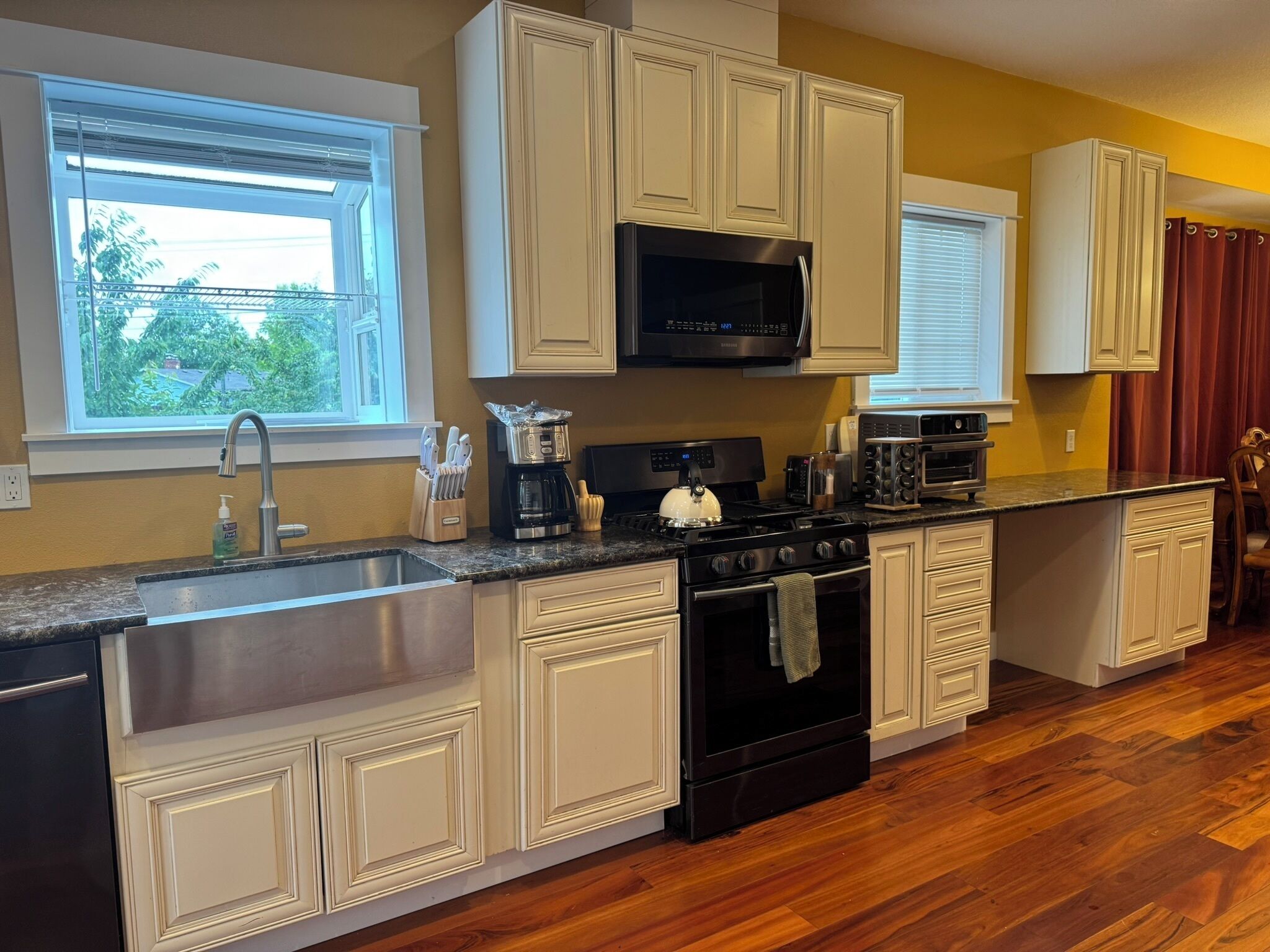 A kitchen with a stainless steel sink, a black stove, a microwave, and a toaster.