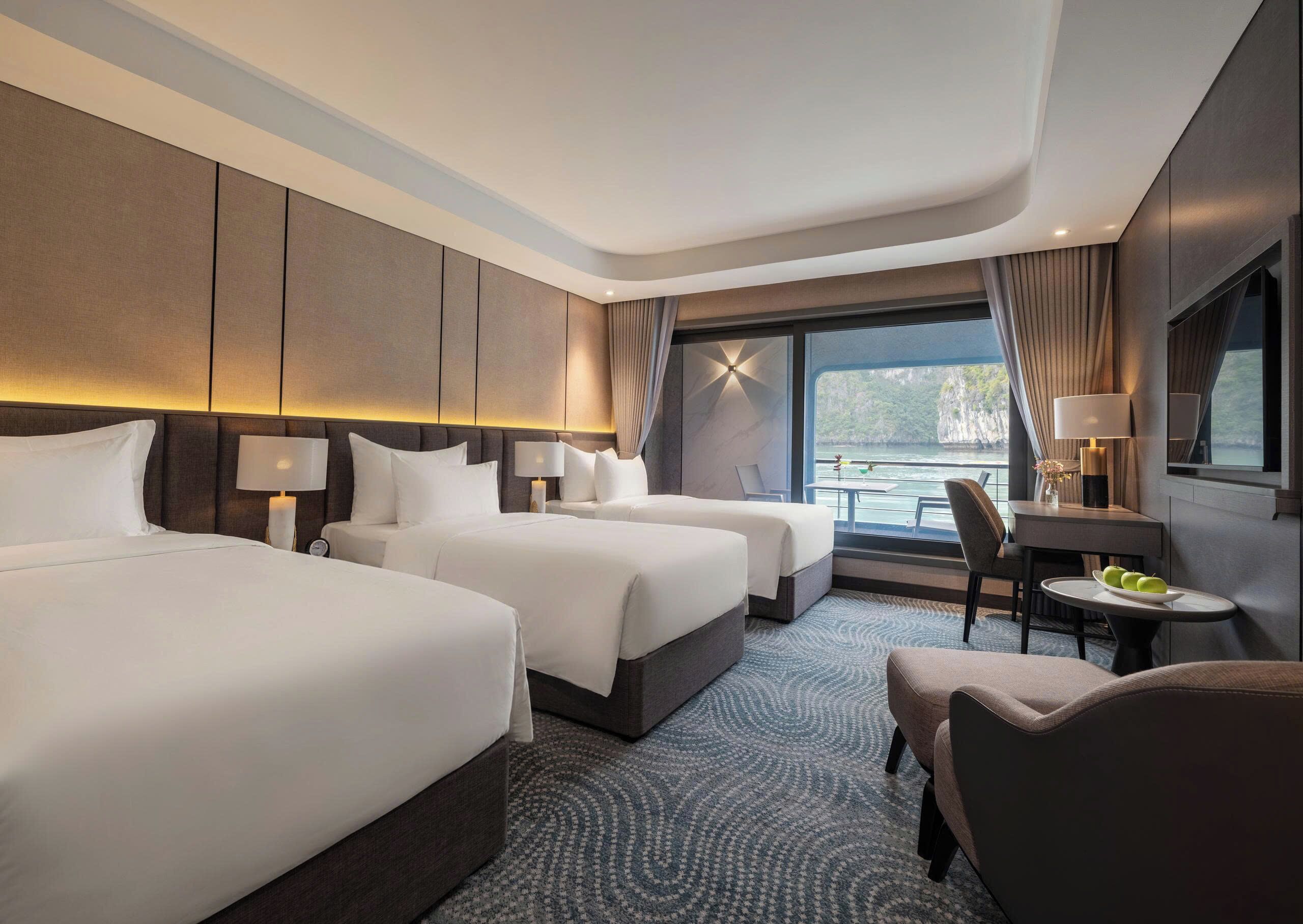 A hotel room with two beds, a desk, a chair, and a view of the sea.