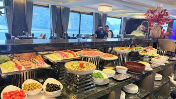 Un buffet proposant une variété de plats, avec une vue sur la mer grâce à de grandes fenêtres.