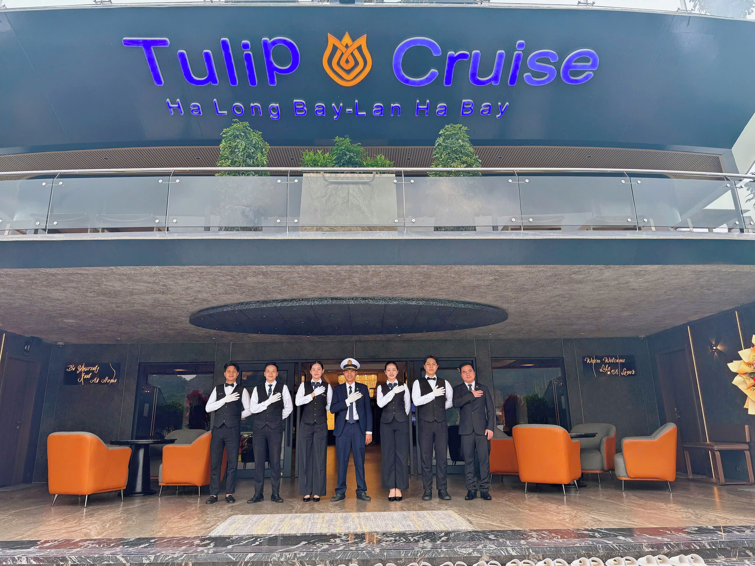 A group of people standing in front of a hotel named 'Tulip Cruise' with a modern design and a sign that reads 'Ha Long Bay-Lan Ha Bay'.