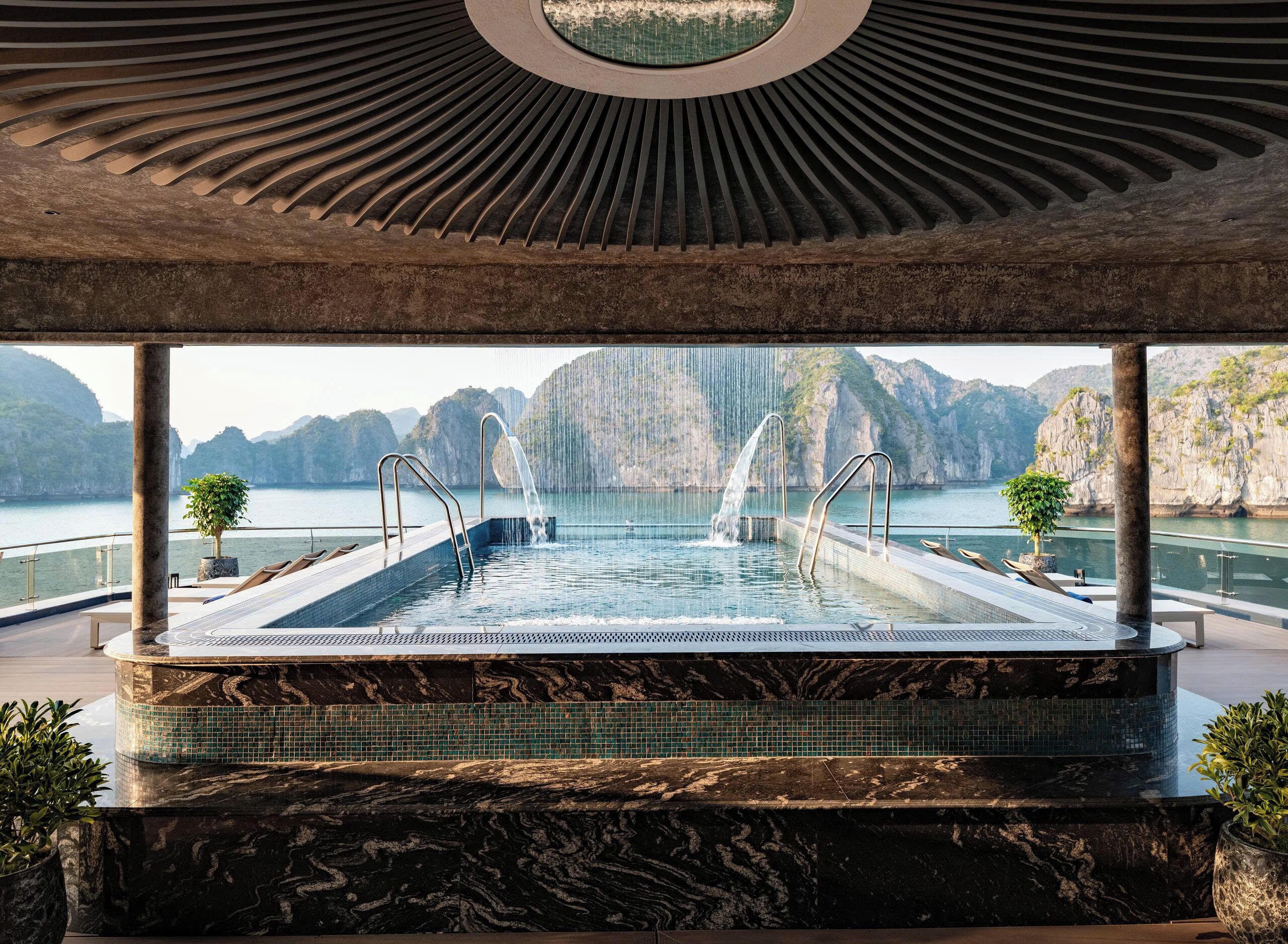 Ein luxuriöser Infinity-Pool mit Wasserfall, umgeben von einer Steinterrasse und Blumentöpfen.