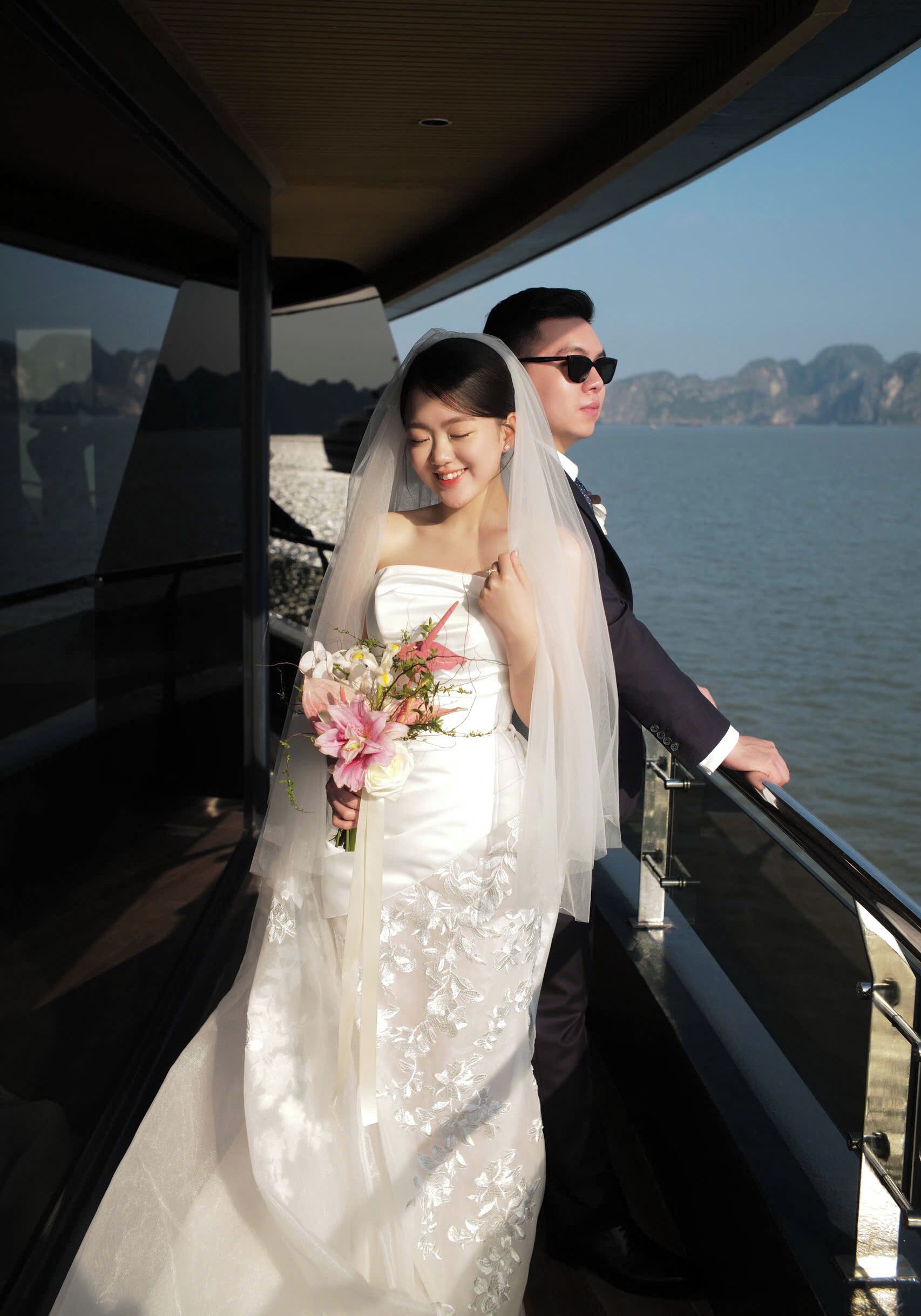 A wedding couple on a boat with a view of the water and distant mountains.