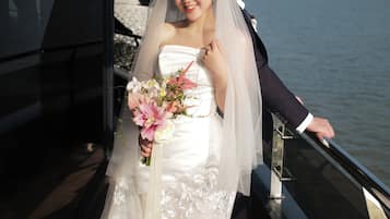 A wedding couple on a boat with a view of the water and distant mountains.