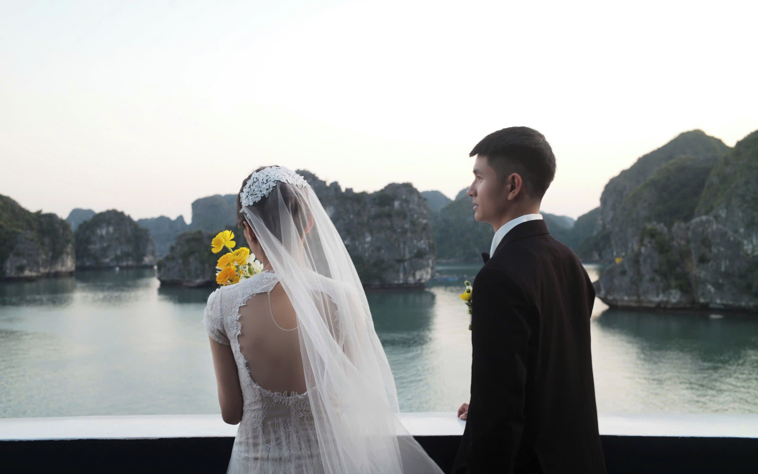 A couple standing by a body of water with rocky cliffs in the background.