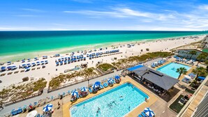 A beach resort with a swimming pool, beach umbrellas, and a view of the ocean.