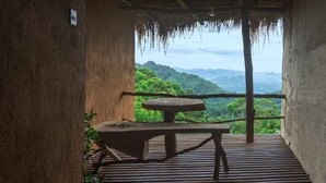 Mesa y banco de madera bajo un tejado de paja, con vistas a un paisaje verde y exuberante.