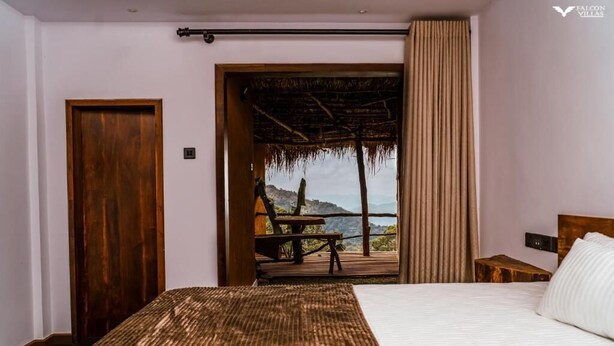 Un dormitorio con una cama grande, una puerta de madera y vista a una playa a través de una puerta abierta.