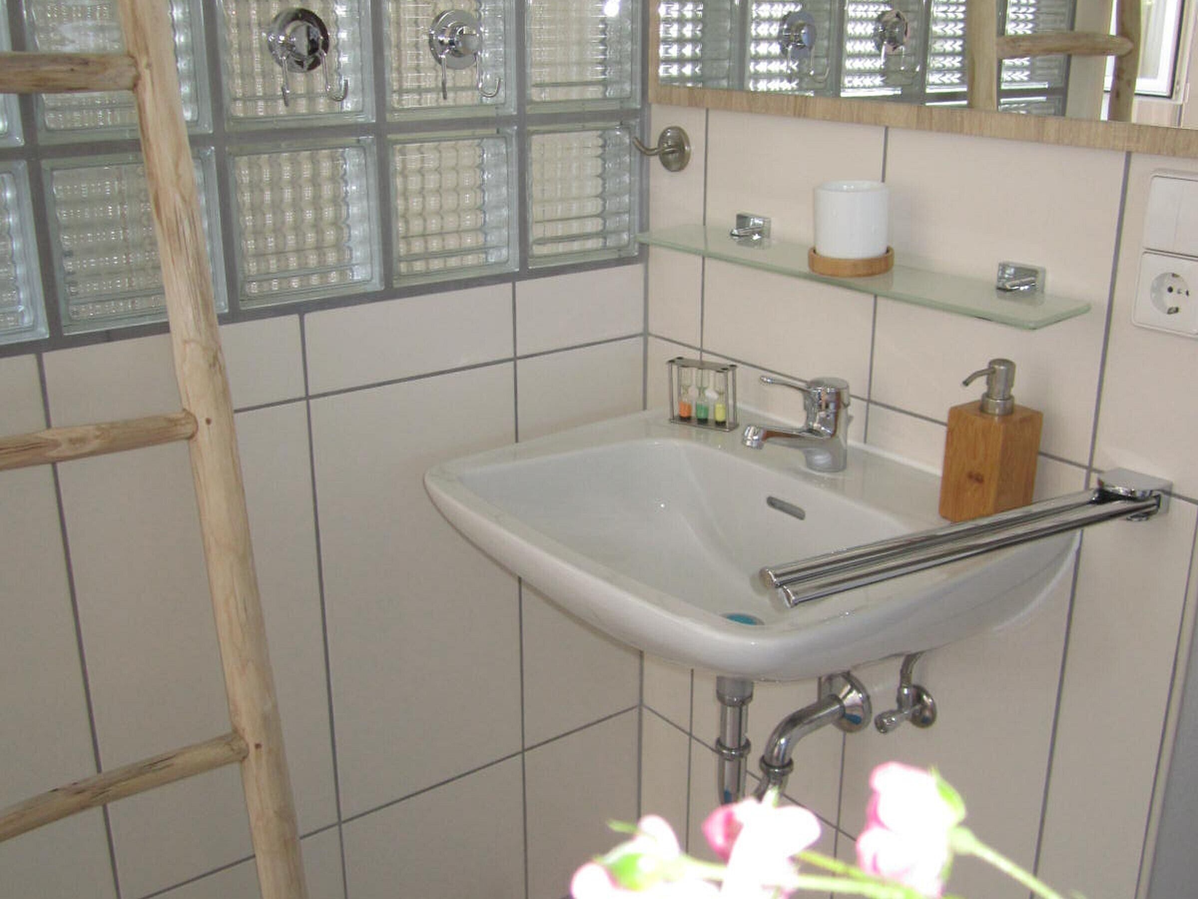 Un bagno con un lavandino bianco, un dispenser di sapone in legno e uno scaffale in vetro con articoli da toilette.