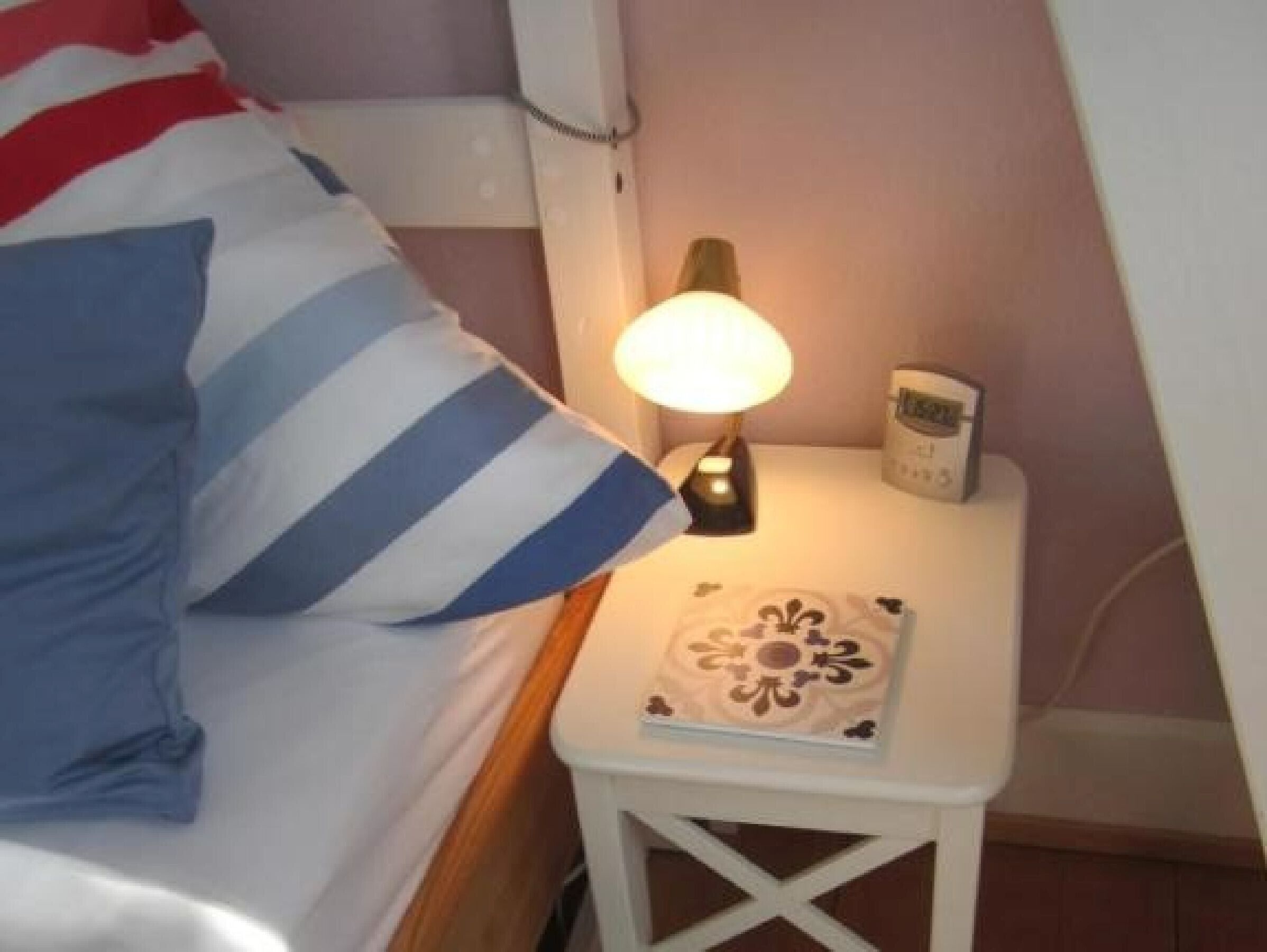 Un llit amb almoiners estriats, una làmpada de nit, una taula petita amb un objecte decoratiu i un telèfon fixat a la paret.