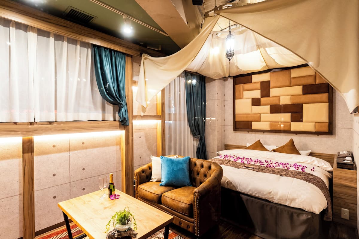 A cozy room with a bed, a leather armchair, a wooden table, and a decorative wall panel.