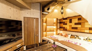 A modern hotel room with a wooden headboard, a flat-screen TV, a dining table with wine glasses, and a canopy bed. - Hotel BaliAn Resort - Shinjuku Forest (Tokyo)
