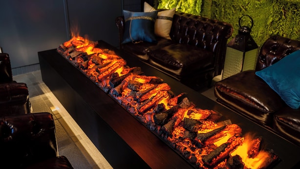A lounge area with a long, rectangular fire feature, leather seating, and a green textured wall. - Hotel BaliAn Resort - Shinjuku Forest (Tokyo)