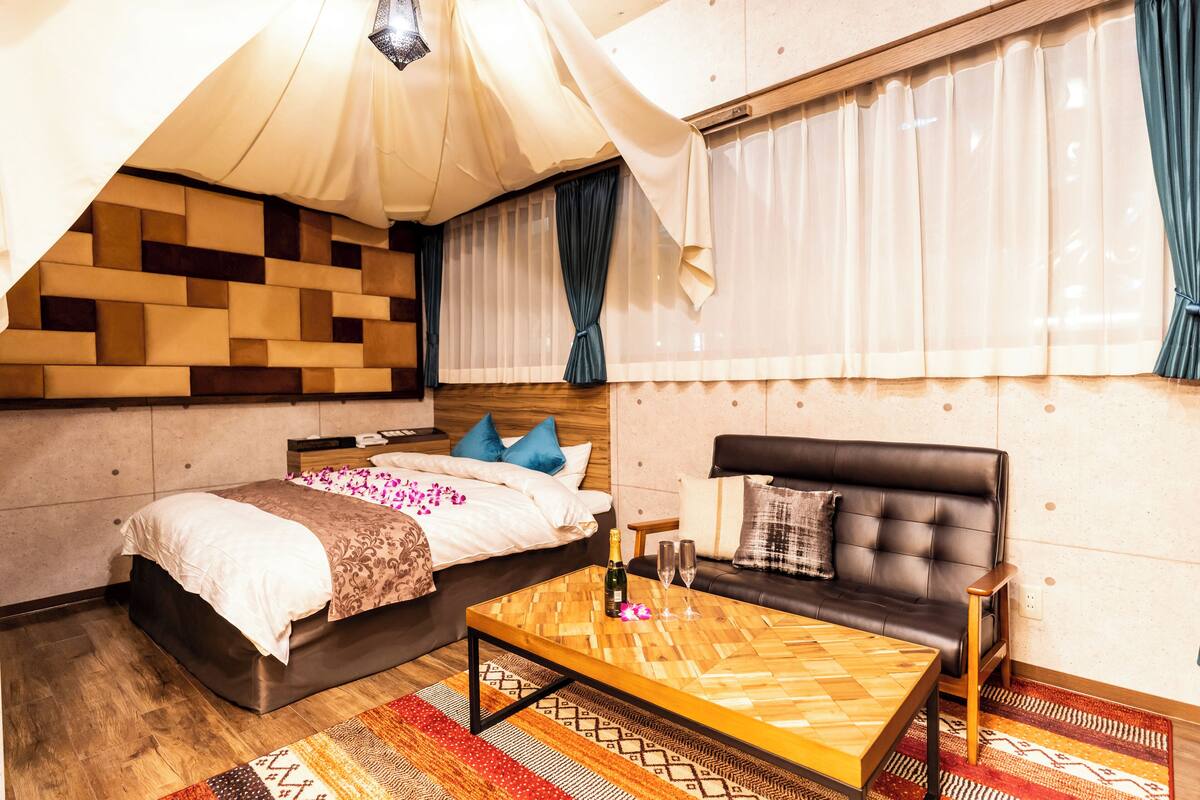 A modern bedroom with a large bed, a sofa, a wooden coffee table, and a patterned rug.