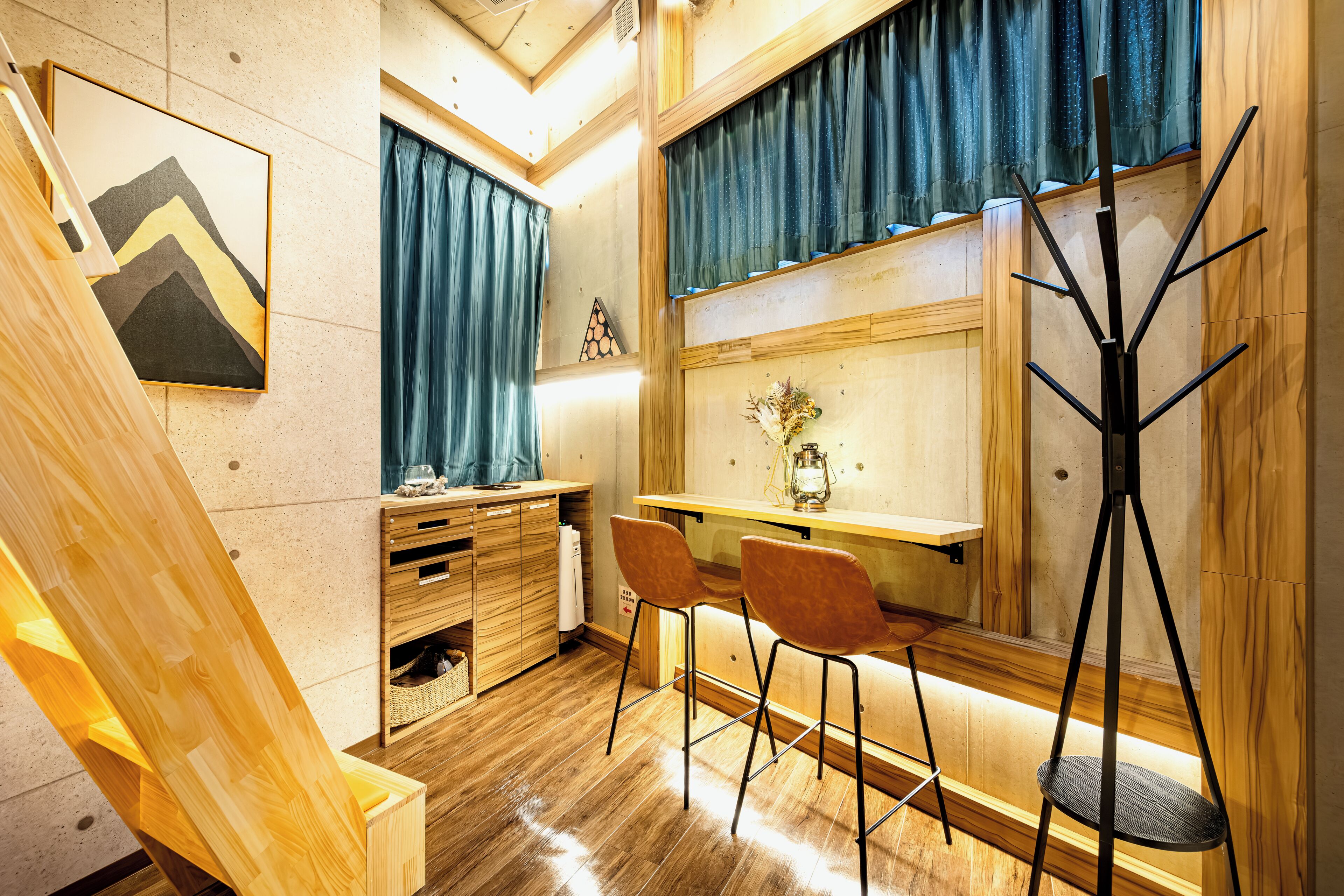 Um quarto com uma escrivaninha de madeira, duas cadeiras, um abajur de tripé, uma janela com cortinas, um quadro na parede e uma escada de madeira.