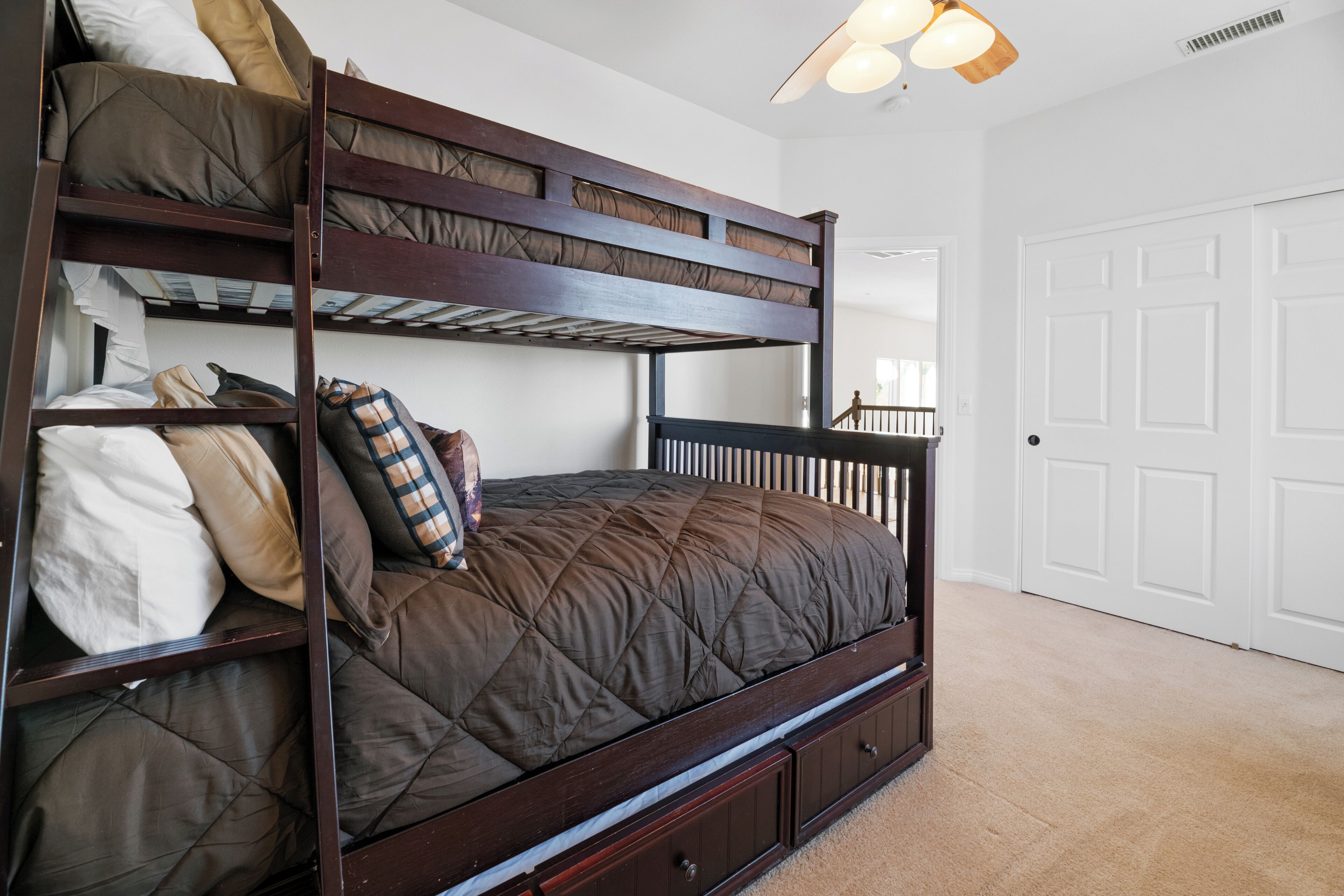 Una cama litera con colchón acolchado, estructura de madera y cabecero. Se ve una puerta blanca al fondo.