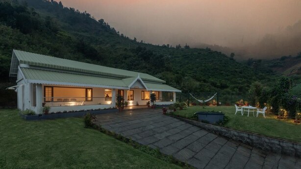 A house with a green roof, a paved driveway, and a garden with outdoor furniture.
