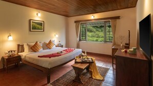 A bedroom with a wooden ceiling, a bed with pillows, a nightstand, a bedside table, a window with curtains, and a TV on a wooden stand.