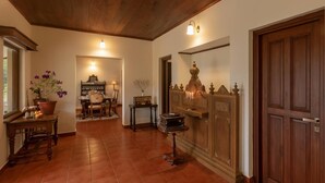 A hallway with a wooden ceiling, a potted plant, a table with a chair, and a decorative cabinet.