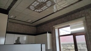 A kitchen with white cabinets, a decorative ceiling, and a window with blinds.