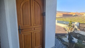 A wooden door with a traditional design, leading to a balcony with a view of a vineyard and a swimming pool.