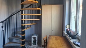 A spiral staircase with wooden steps and black handrails, a wooden door, a small table with a bench, and a window with blinds.
