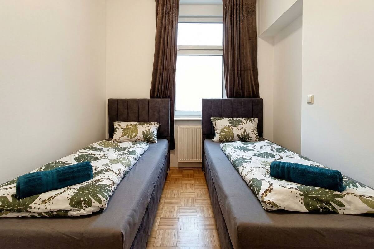 A small room with two single beds, each with a headboard, a window with curtains, and a radiator.