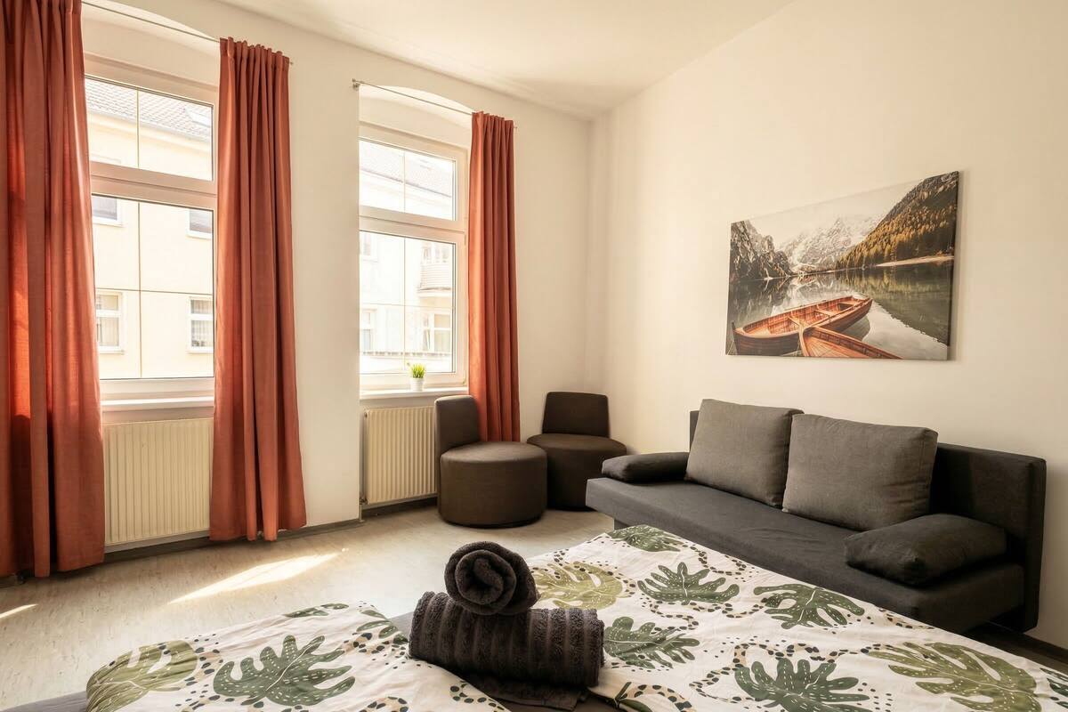 A bedroom with a bed, a sofa, a chair, and a window with curtains.