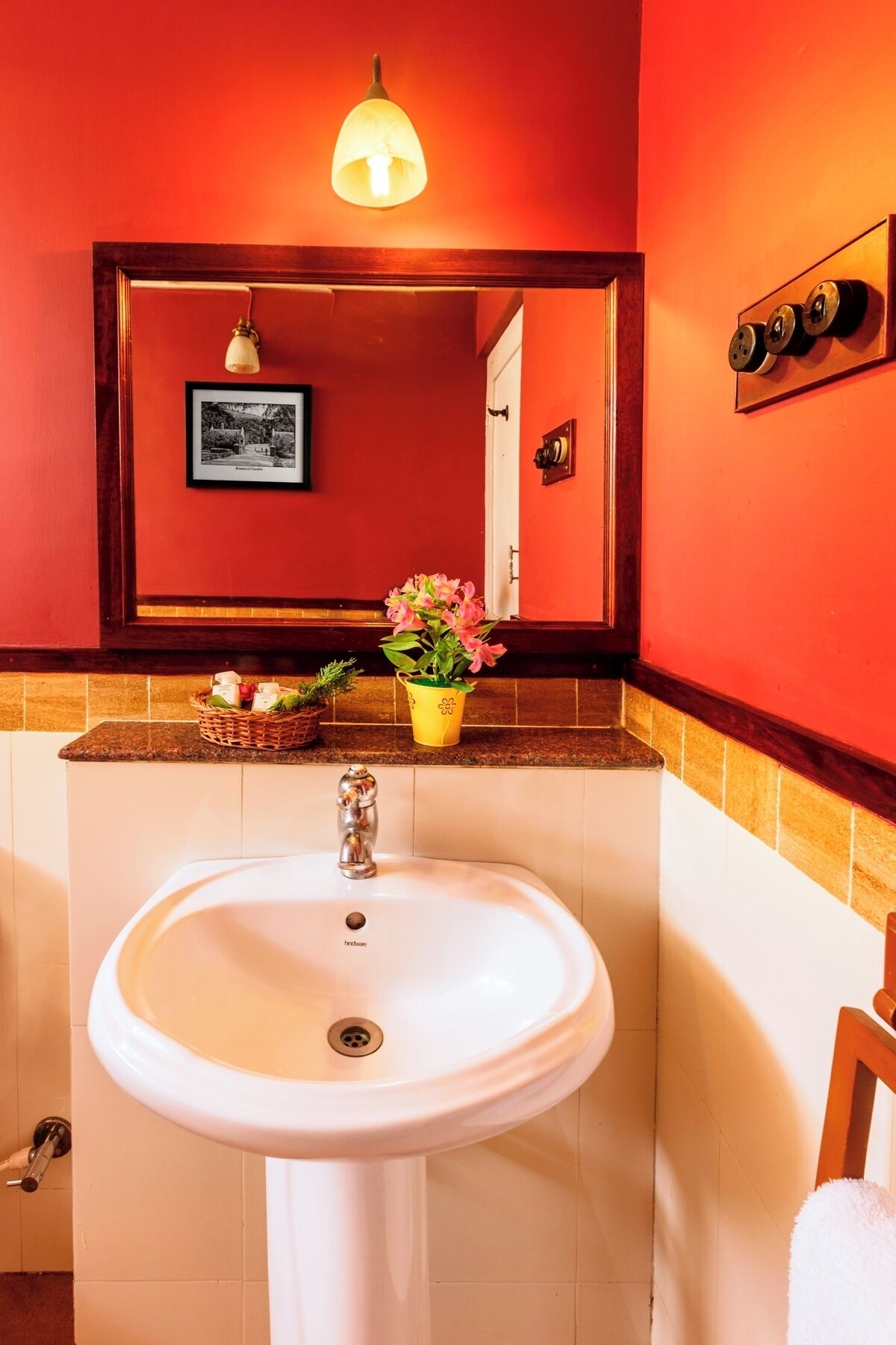 A bathroom with a white sink, a mirror above it, a red wall, and a yellow flower vase on the countertop.