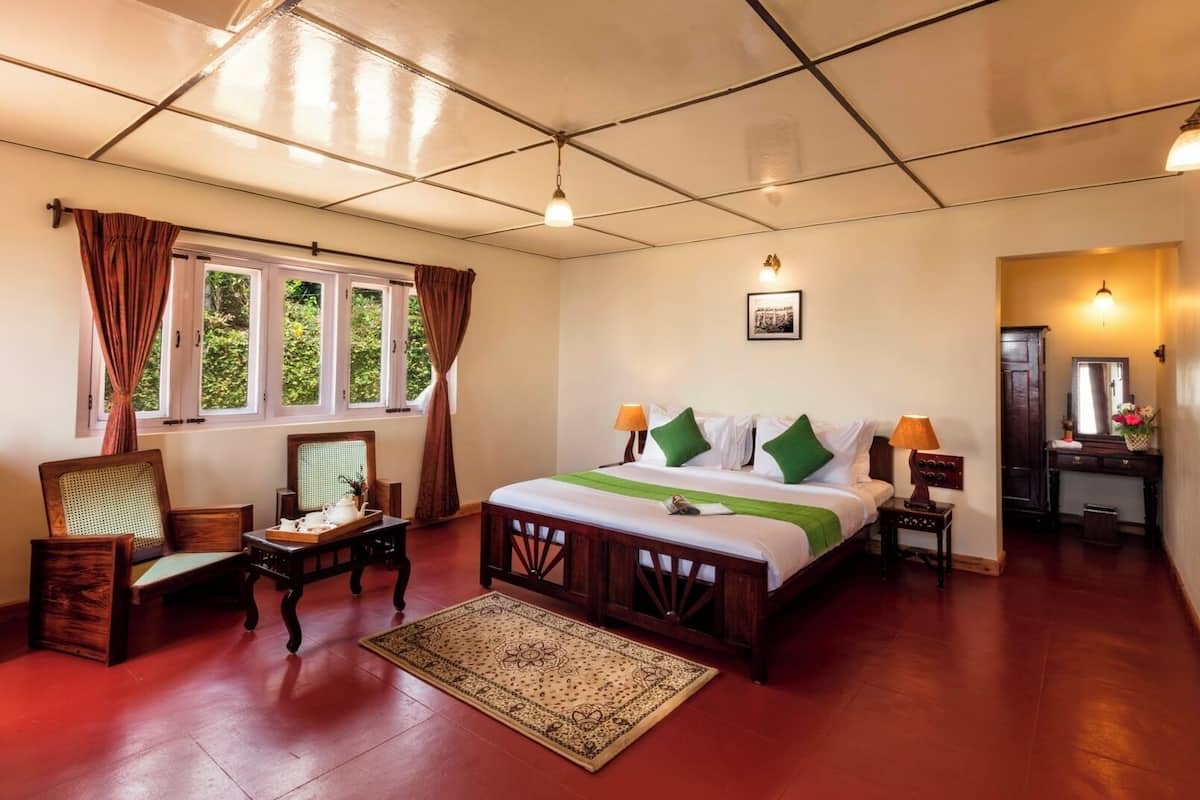 Une chambre d’hôtel avec un grand lit, un coin salon comprenant une chaise et une table, et une vue sur la verdure par la fenêtre.