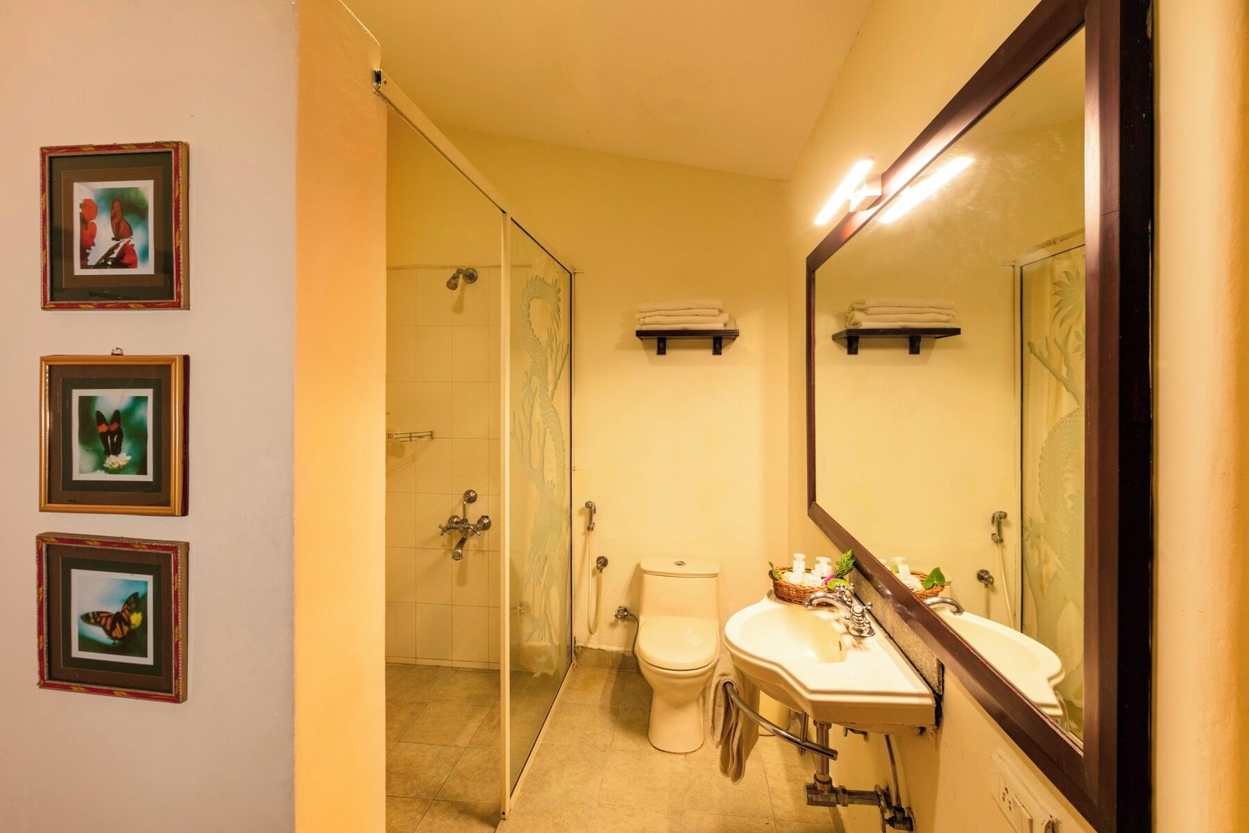 A bathroom with a toilet, sink, and shower. There are framed pictures on the wall.