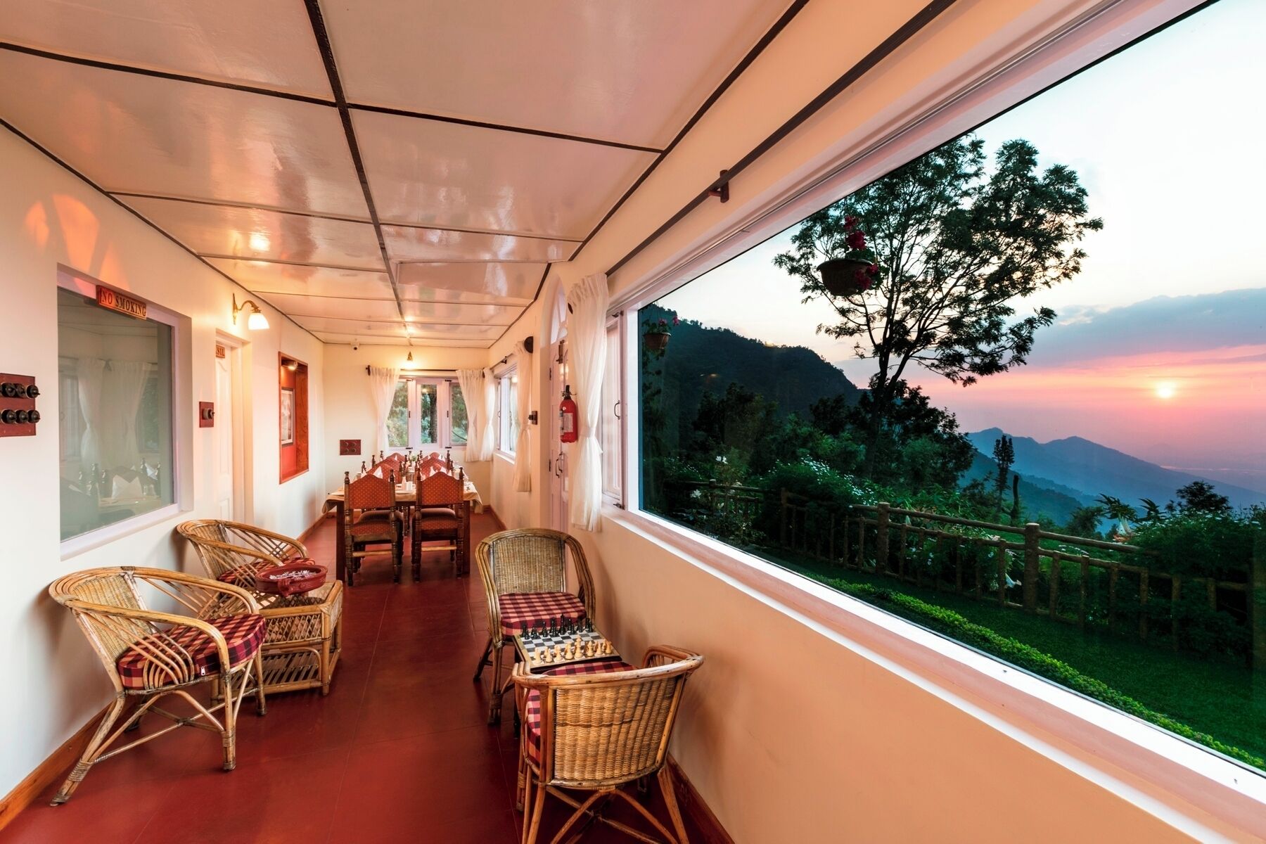 A dining area with wicker chairs and a table set for two, a window with a view of a mountainous landscape, and a 'No Smoking' sign on the wall.