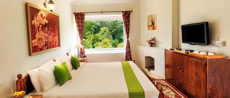 A hotel room with a bed, a TV, a wooden cabinet, a window with curtains, and a framed picture on the wall.