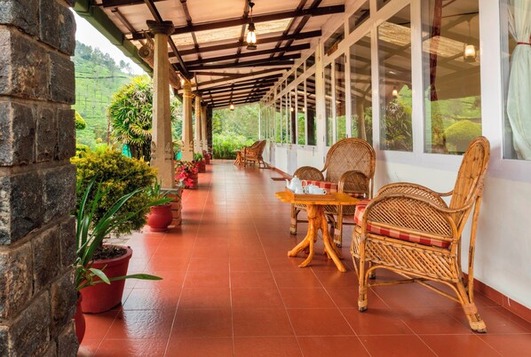 A covered terrace with wicker furniture and potted plants. - Teanest by Nature Resorts and Stay  (Coonoor)