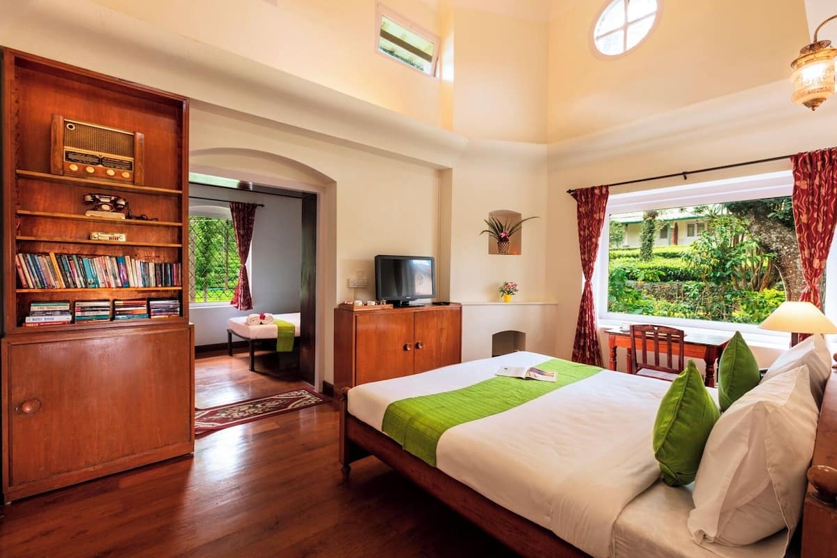 Une chambre d’hôtel avec un lit en bois, une télévision, une bibliothèque et une fenêtre donnant sur un paysage verdoyant.