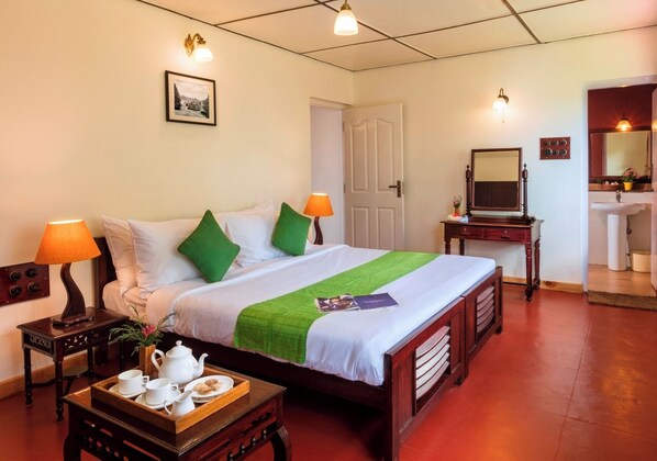 A neatly arranged hotel room with a bed, bedside tables, a nightstand, a dresser, a mirror, and a bathroom visible through an open door.