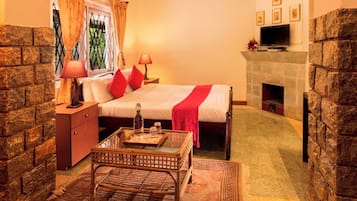 A cozy bedroom with a stone fireplace, a bed with red pillows, a nightstand with lamps, and a small table with a bottle and glasses.