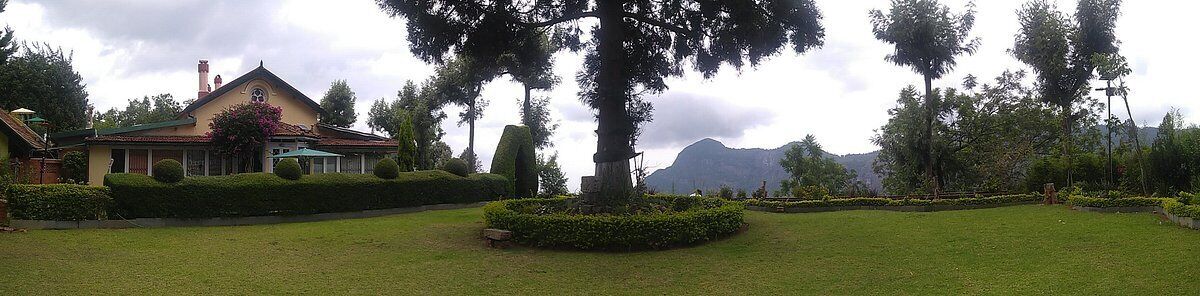 Una casa amb un jardí ben cuidat, un arbre gran i una muntanya al fons.
