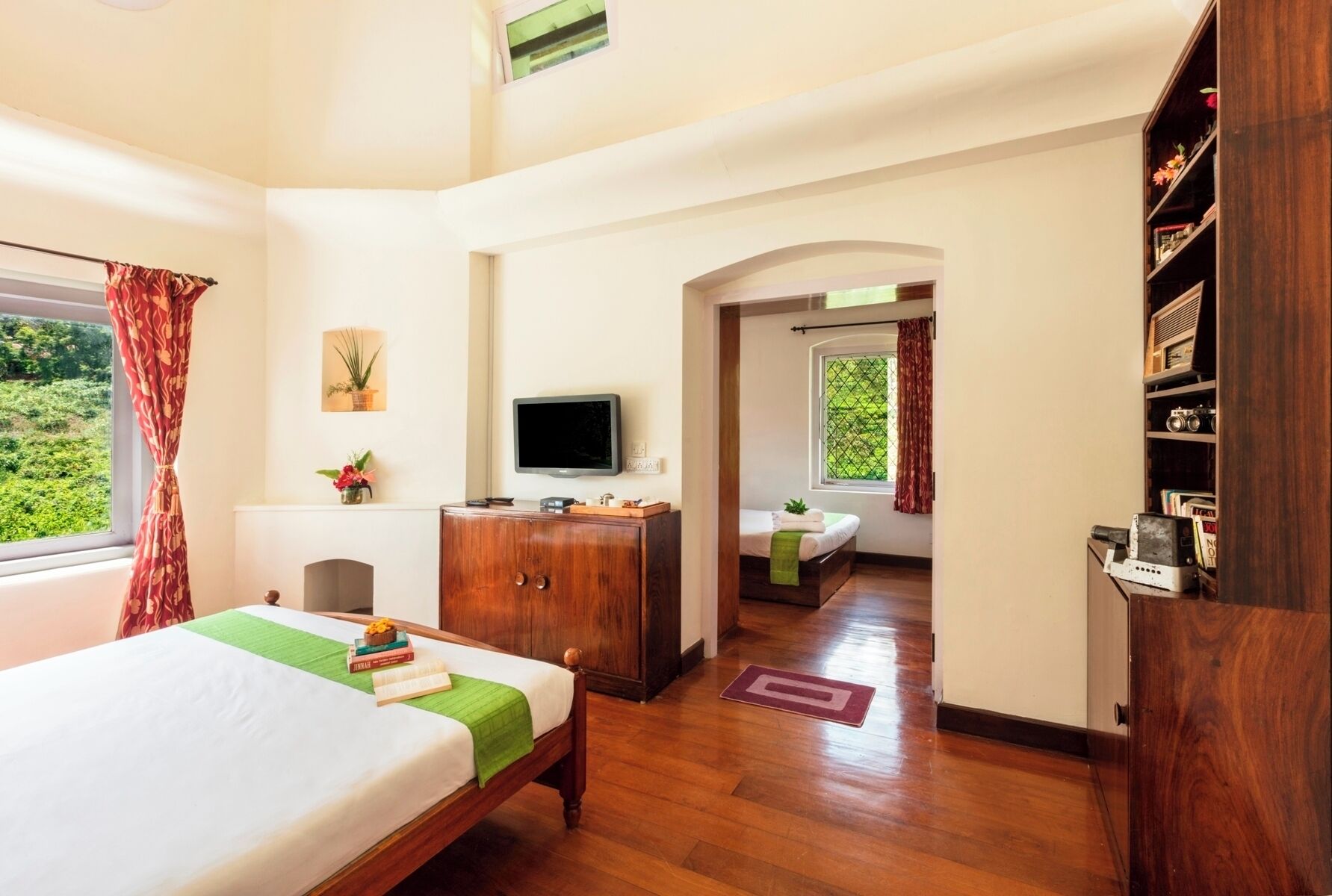 Un dormitorio con cama, televisor, aparador de madera, estantería y ventana con cortinas.