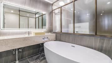 A modern bathroom with a freestanding bathtub, a large mirror with integrated lighting, and a window with frosted glass.