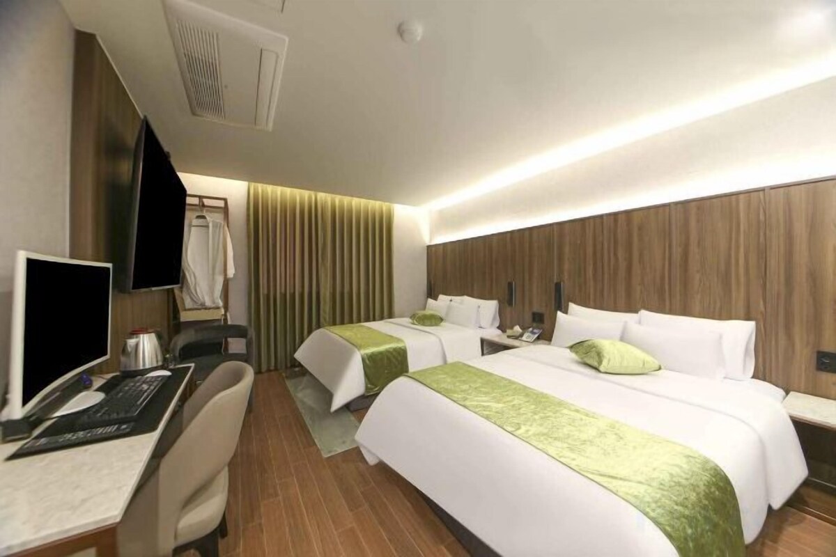 A hotel room with two beds, a desk with a computer, a chair, and a TV.
