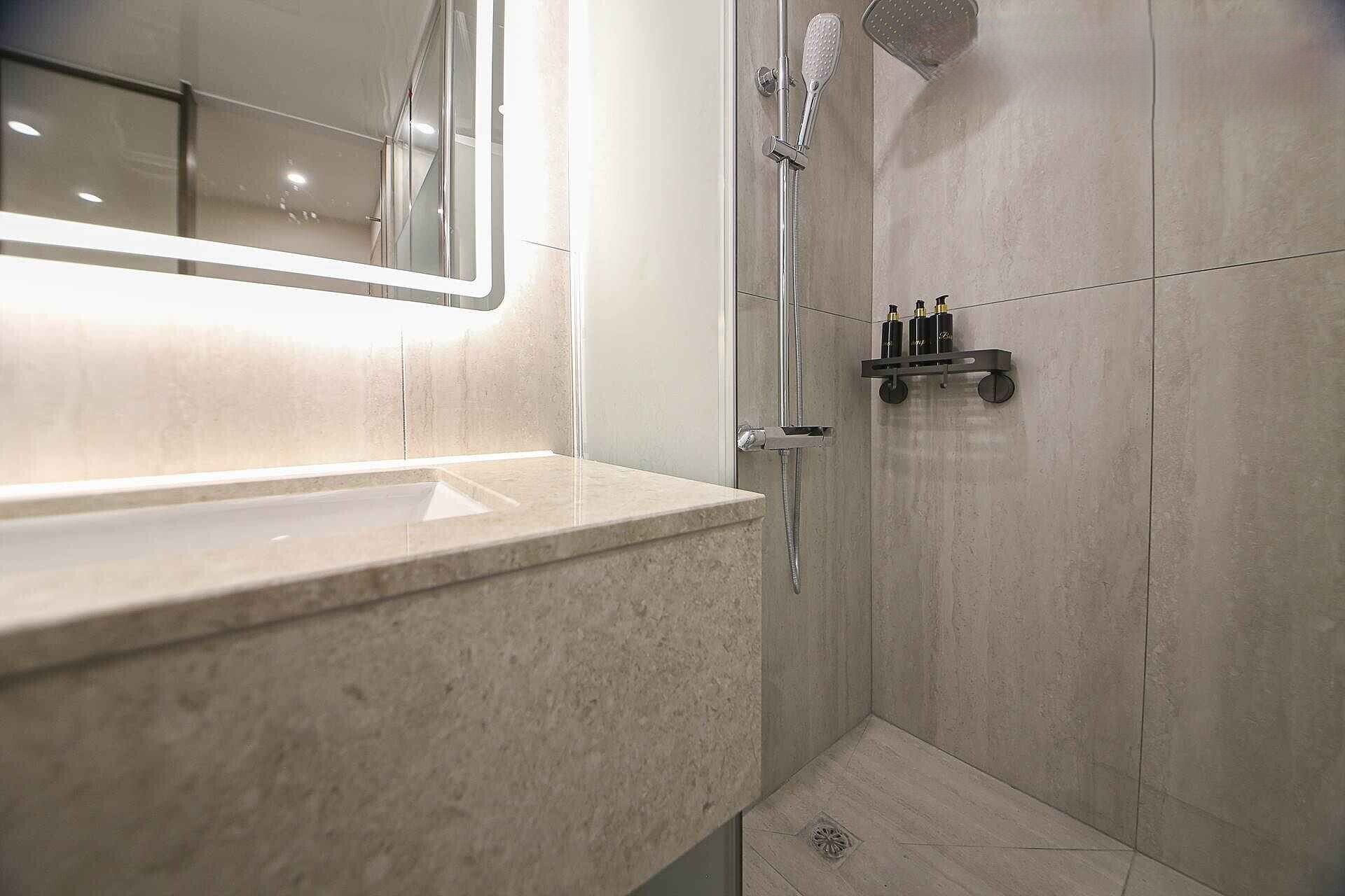 Uma casa de banho moderna com lavatório de mármore, chuveiro manual e prateleira com artigos de higiene pessoal.
