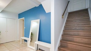 Una escalera de madera con escalones que conducen a un rellano, un banco blanco y una pared azul con un espejo de marco blanco.