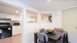 Cocina compacta con microondas, estufa y armarios. Hay un comedor con mesa y sillas, y una puerta que da a otra habitación.