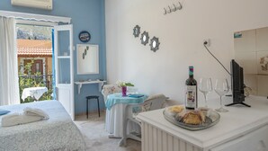 A room with a bed, a table with a bottle and glasses, a chair, and a view of the outside. - Apartment 'Studio 1' with Mountain View, Wi-Fi and Air Conditioning (Kalymnos)