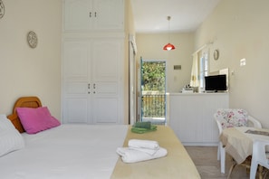 A bedroom with a bed, a desk, a chair, a TV, and a balcony with a view.
