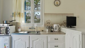 Uma cozinha com janela, pia, fogão, micro-ondas, geladeira, cafeteira e televisão.